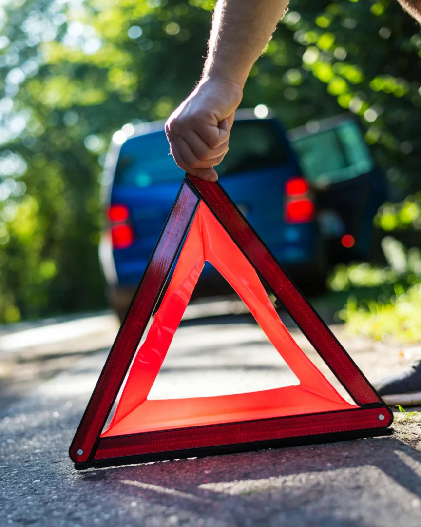 Hand stellt rotes Warndreieck vor blauem Fahrzeug auf – Unfallstelle absichern
